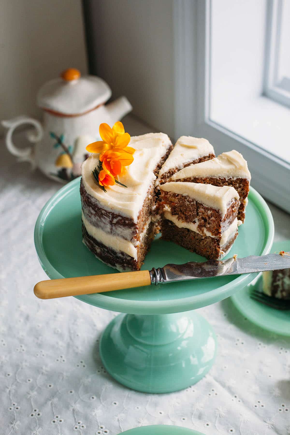 A spiced carrot cake with pineapple cut into slices on a green cake stand.