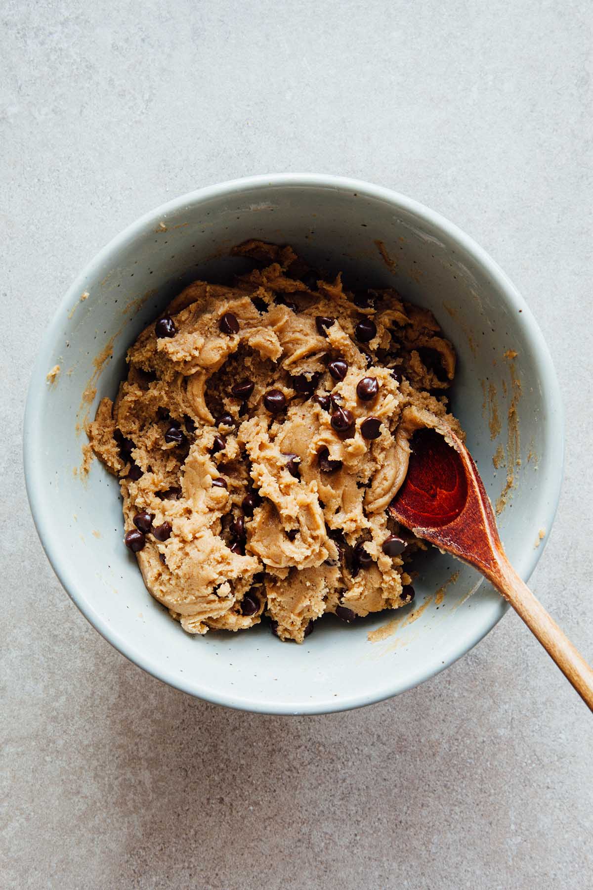 A bowl of cookie dough with a wooden spoon.