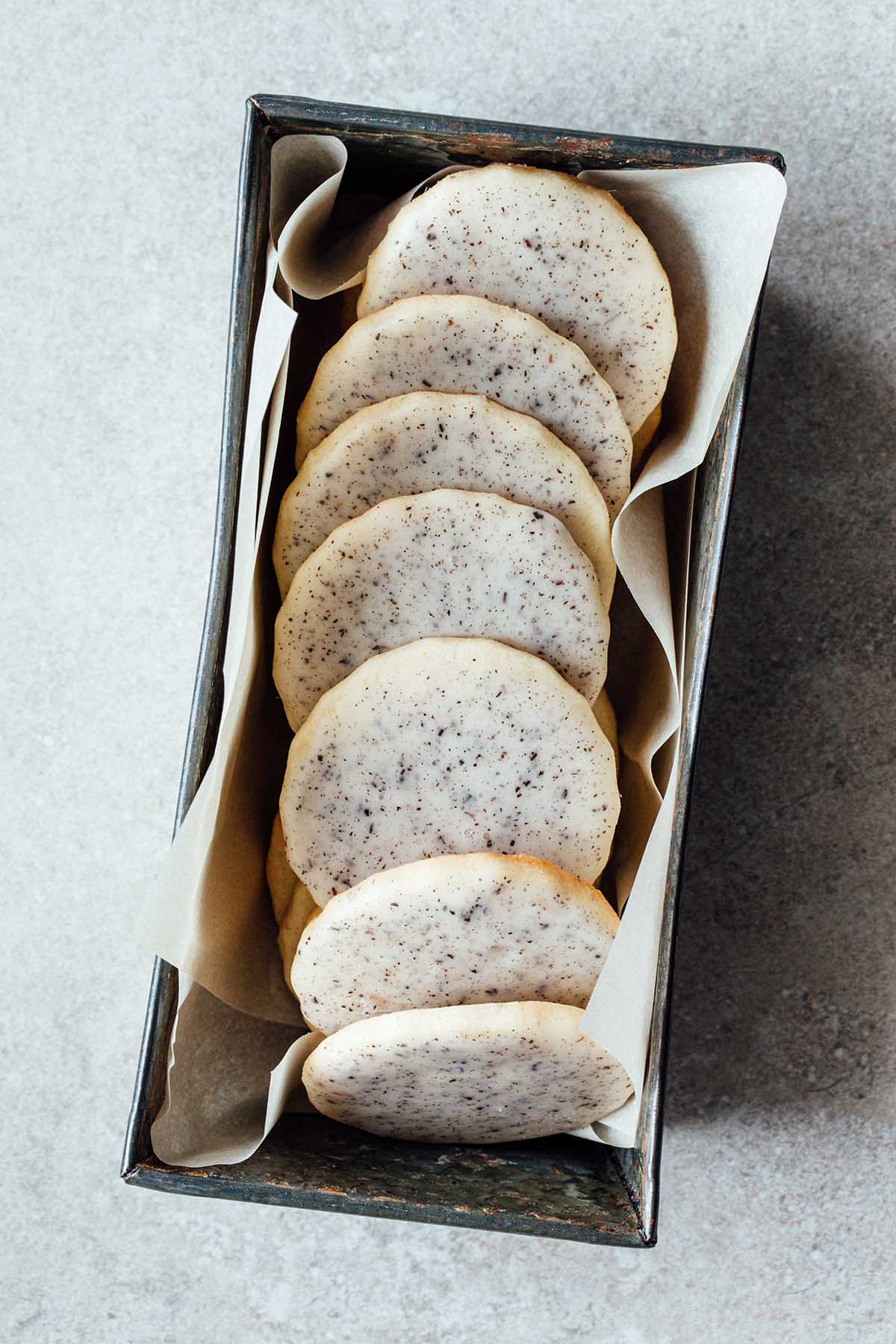 Lavender sugar cookies stacked in a metal tin lined with parchment paper.