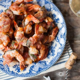 A plate of grilled shrimp with fresh sage and pancetta on a blue and white plate.