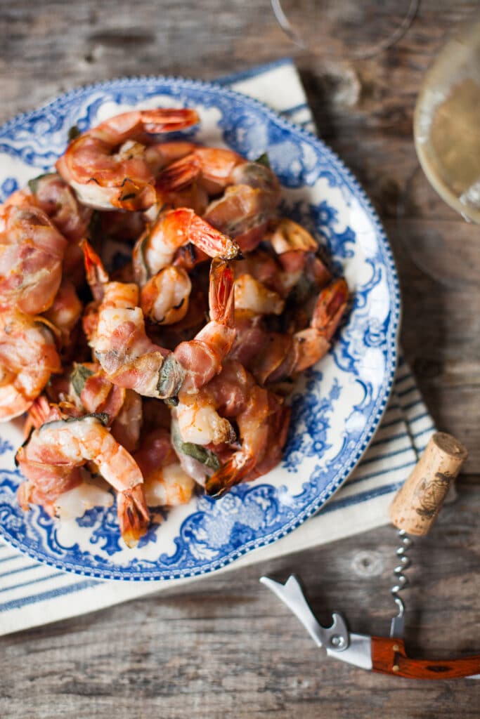 A plate of grilled shrimp with fresh sage and pancetta on a blue and white plate.