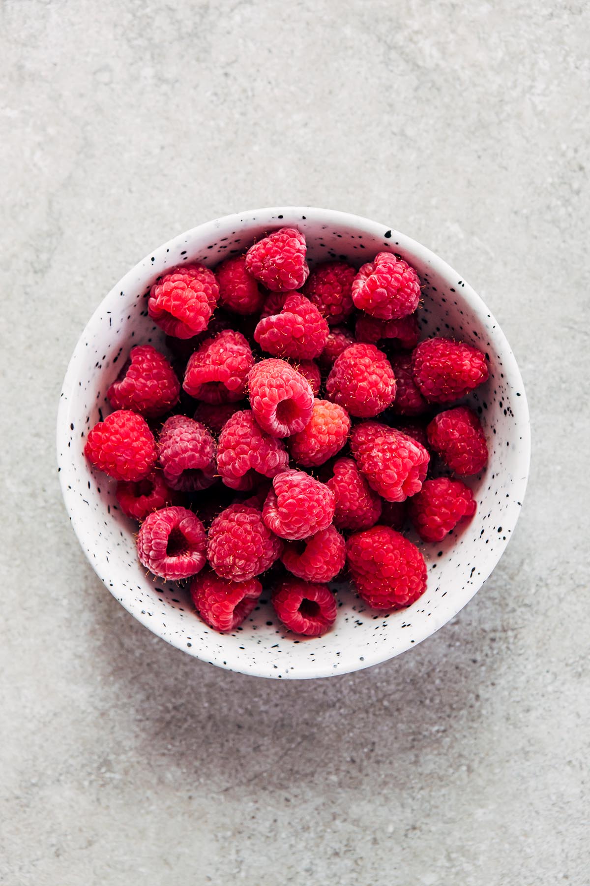 A small bowl of raspberries on a stone surface.