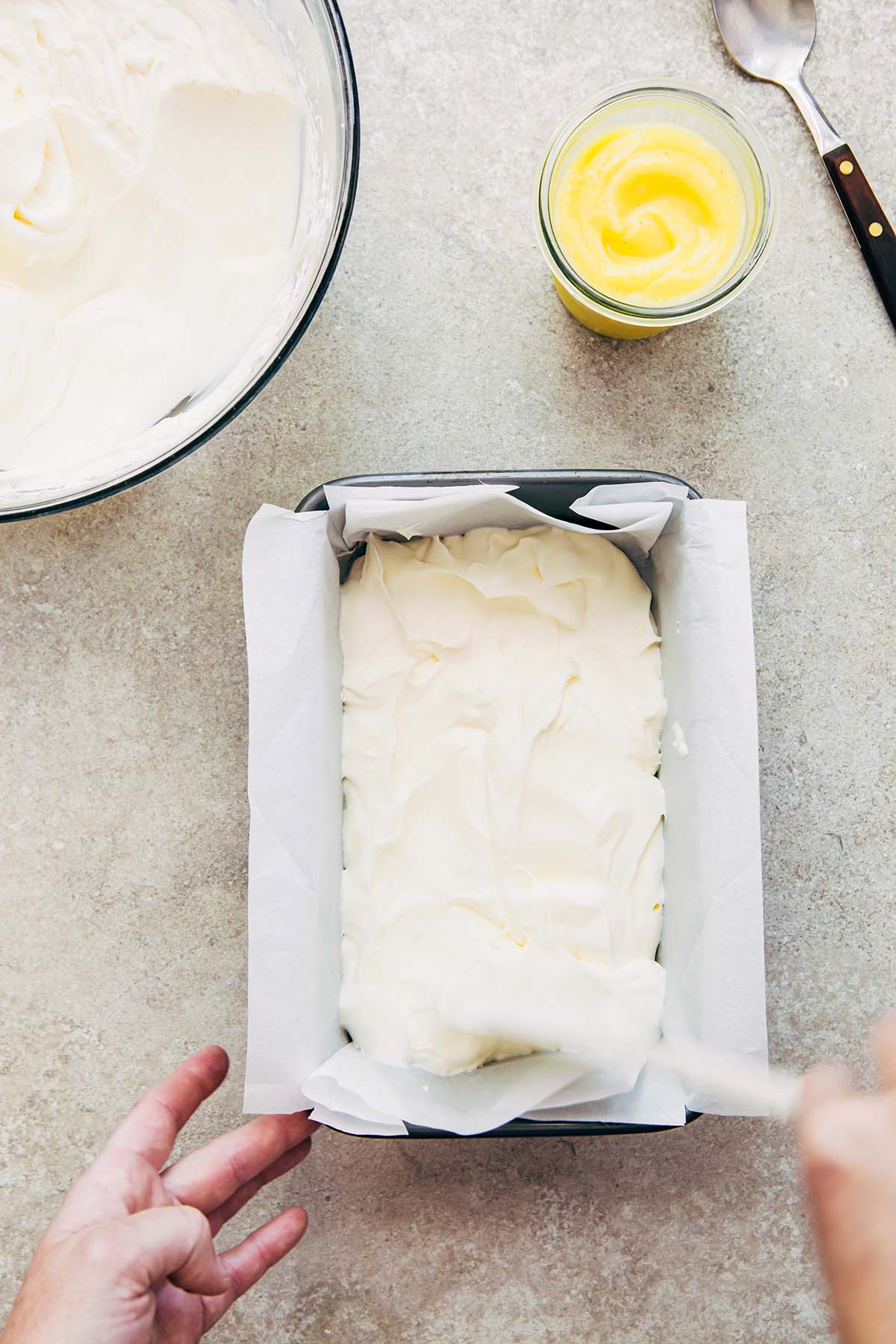 A hand spreading whipped cream in a loaf tin.