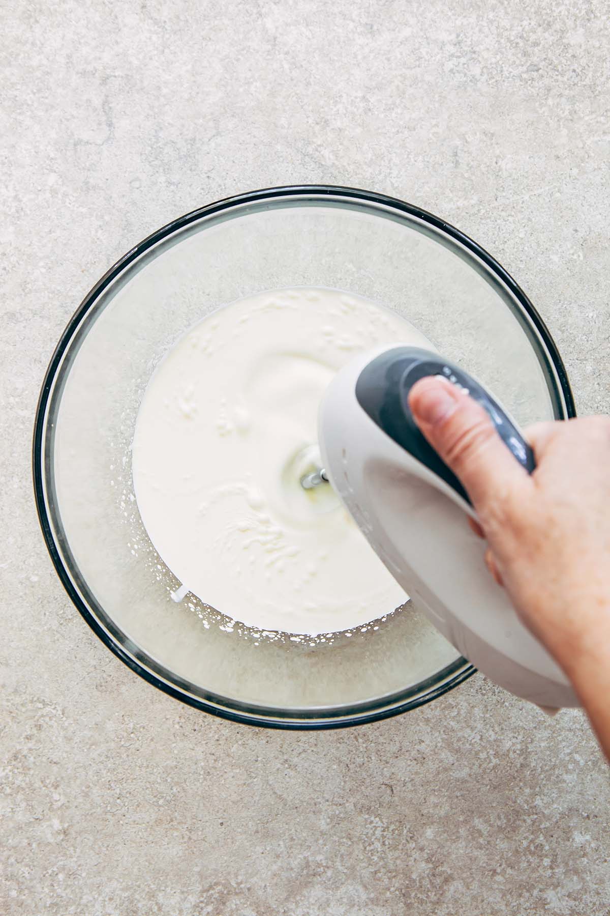 A hand using a hand mixer to whip cream.