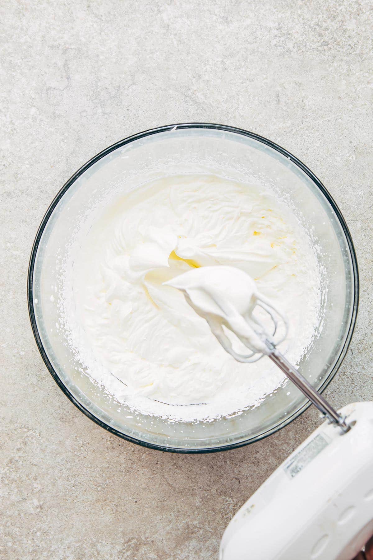 A large glass bowl of whipped cream and the beaters of a hand mixer showing the stiffness of the cream.