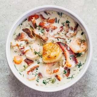 Overhead shot of a bowl of nova Scotia seafood chowder loaded with lobster, haddock, shrimp, potatoes, and bacon, with one golden pan-seared scallop on top.