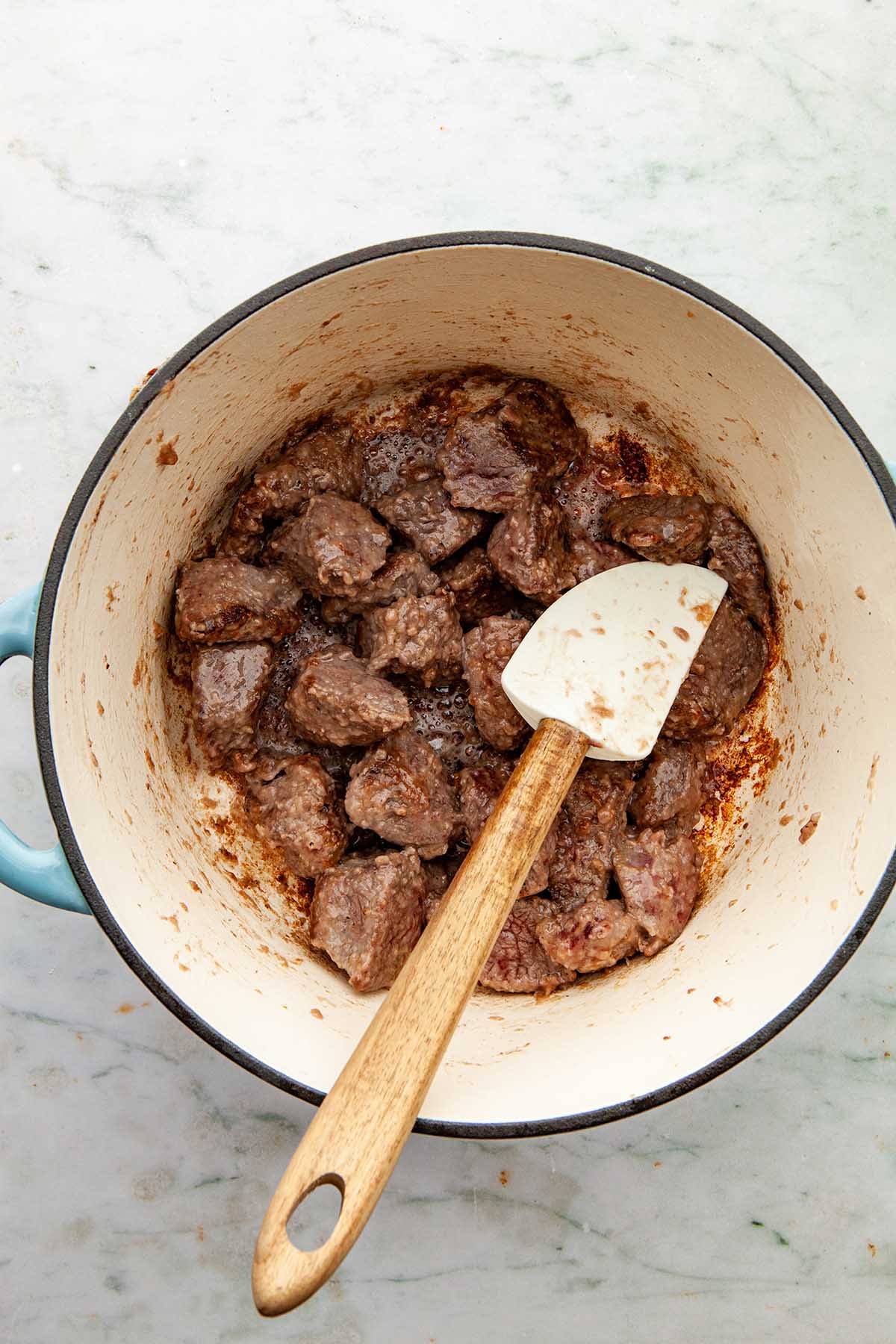 Browned beef cubes in a cast iron enameled pot.