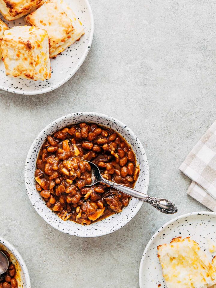 Bowls of homemade molasses baked beans and plates of cheese tea biscuits on the side.
