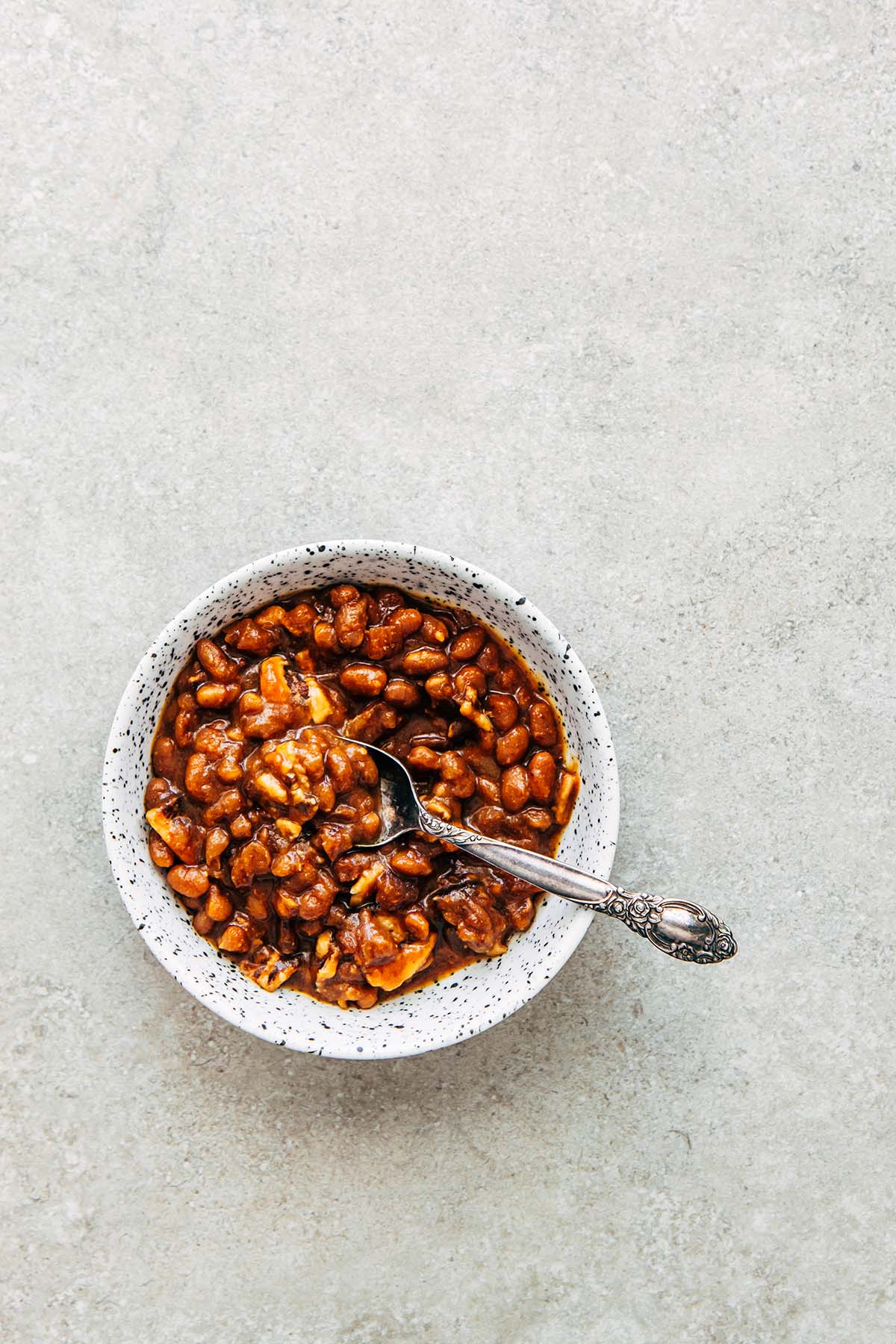 A bowl of beans with a spoon on a stone surface.