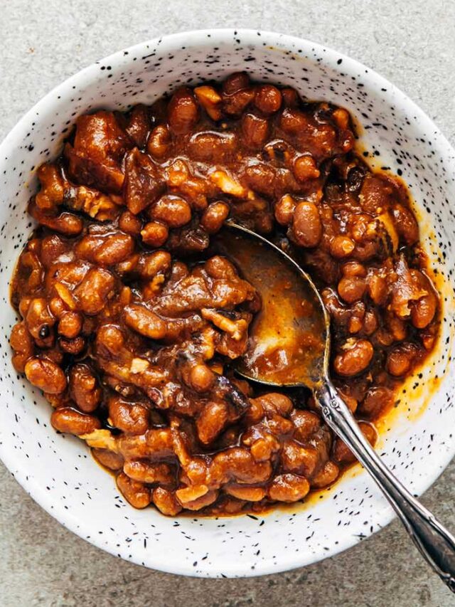 A white speckled bowl of baked beans on a stone surface.