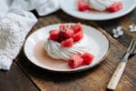 Horizontal photo of a pavlova shell on a plate topped with chunks of watermelon, fresh mint, and lime juice.