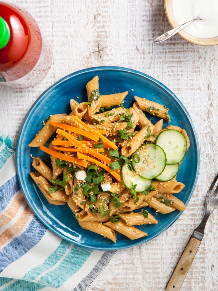 Easy sesame noodles on a blue plate topped with carrot, green onion, and cucumber.