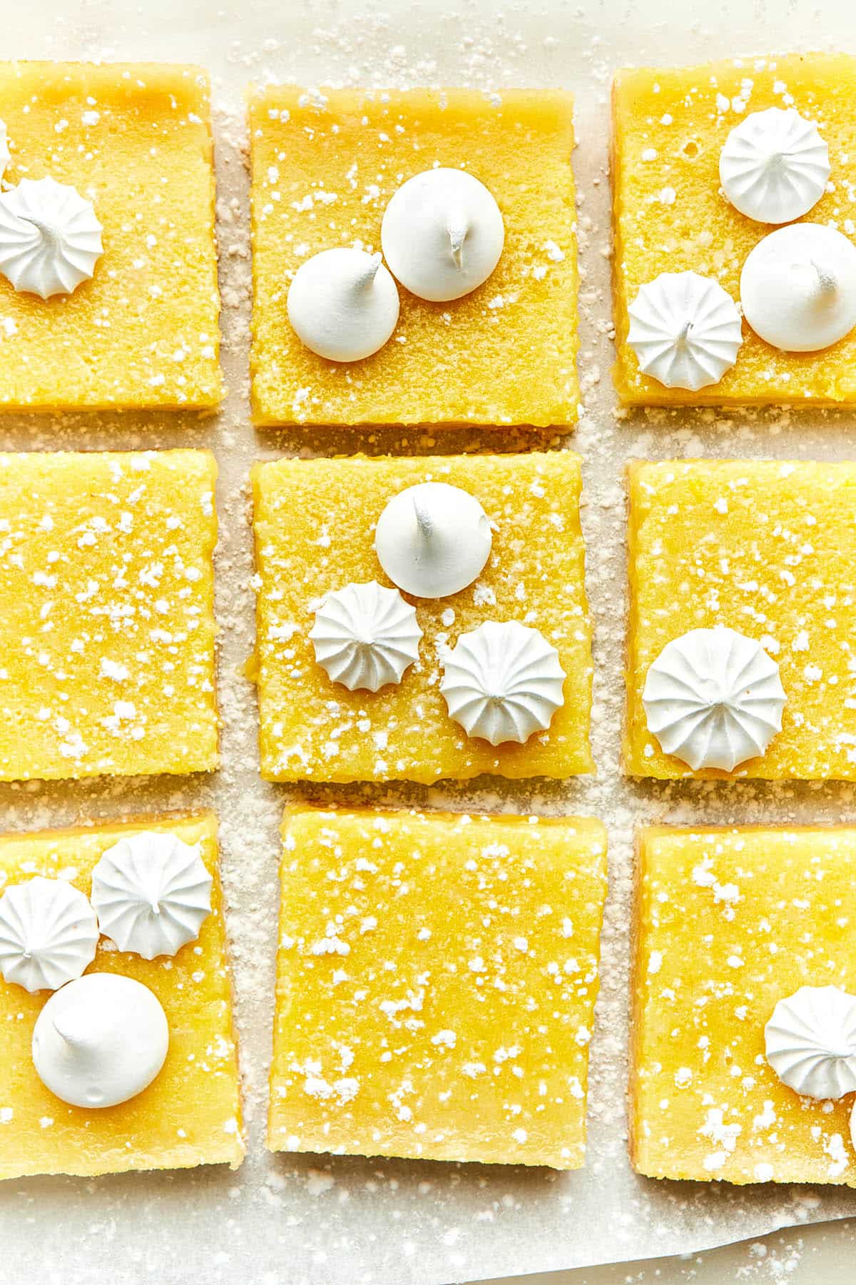 Sliced lemon bars topped with a sprinkle of powdered sugar and two styles of mini meringues.