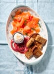 A platter of salmn gravlax, pickled red onion, toasted brown bread, and aioli with sesame seeds.