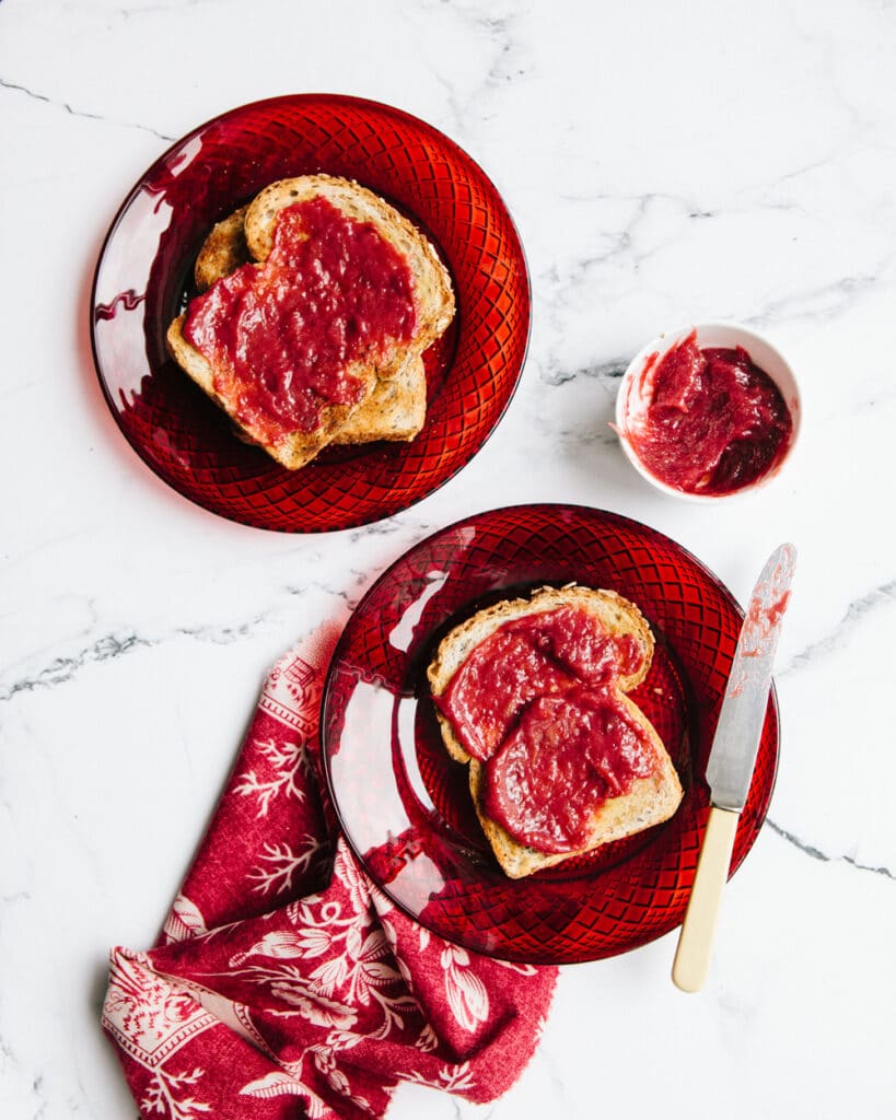 Two slices of toast smeared with maple rhubarb jam on two red glass plate.