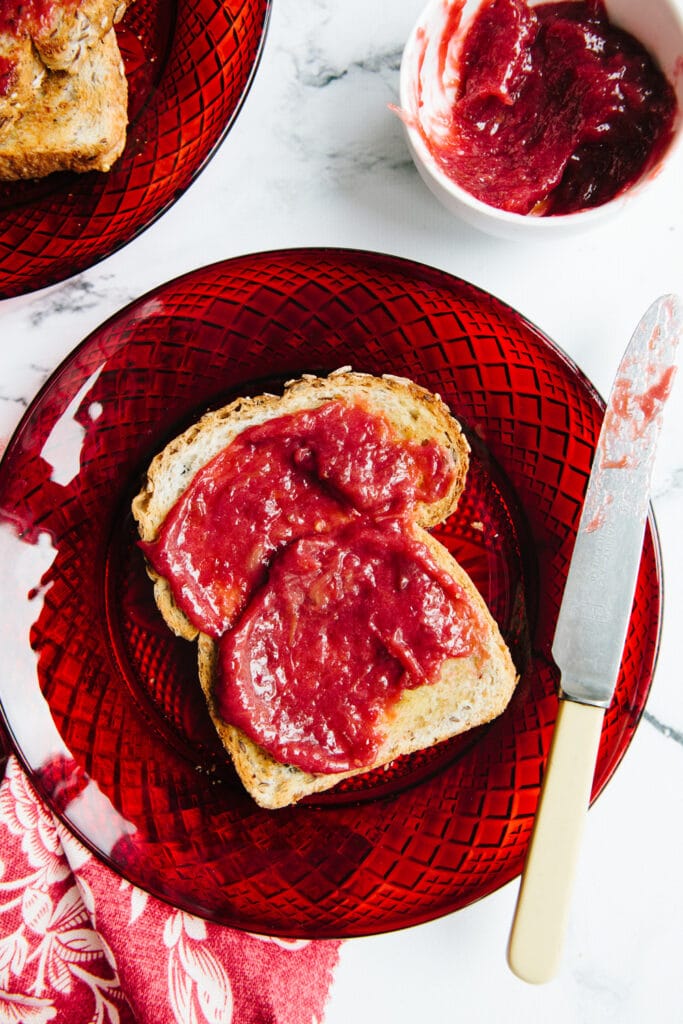 A slice of toast smeared with maple rhubarb jam on a red glass plate.