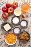 All of the ingredients for apple cider cornflake crisp laid out in dishes on a flowery tablecloth.