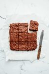Nine double chocolate buckwheat brownies on a sheet of parchment paper alongside a knife
