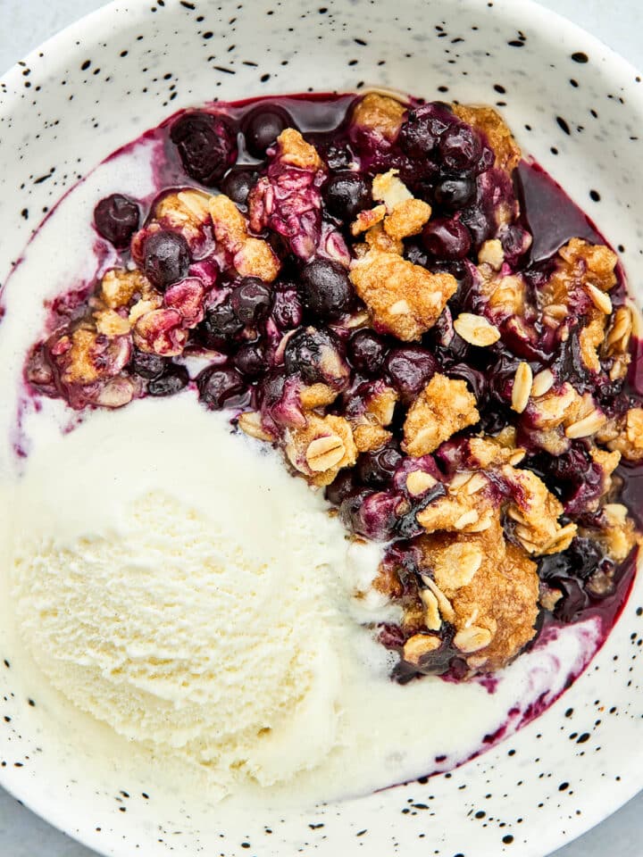 Wild blueberry crisp in a bowl with ice cream.