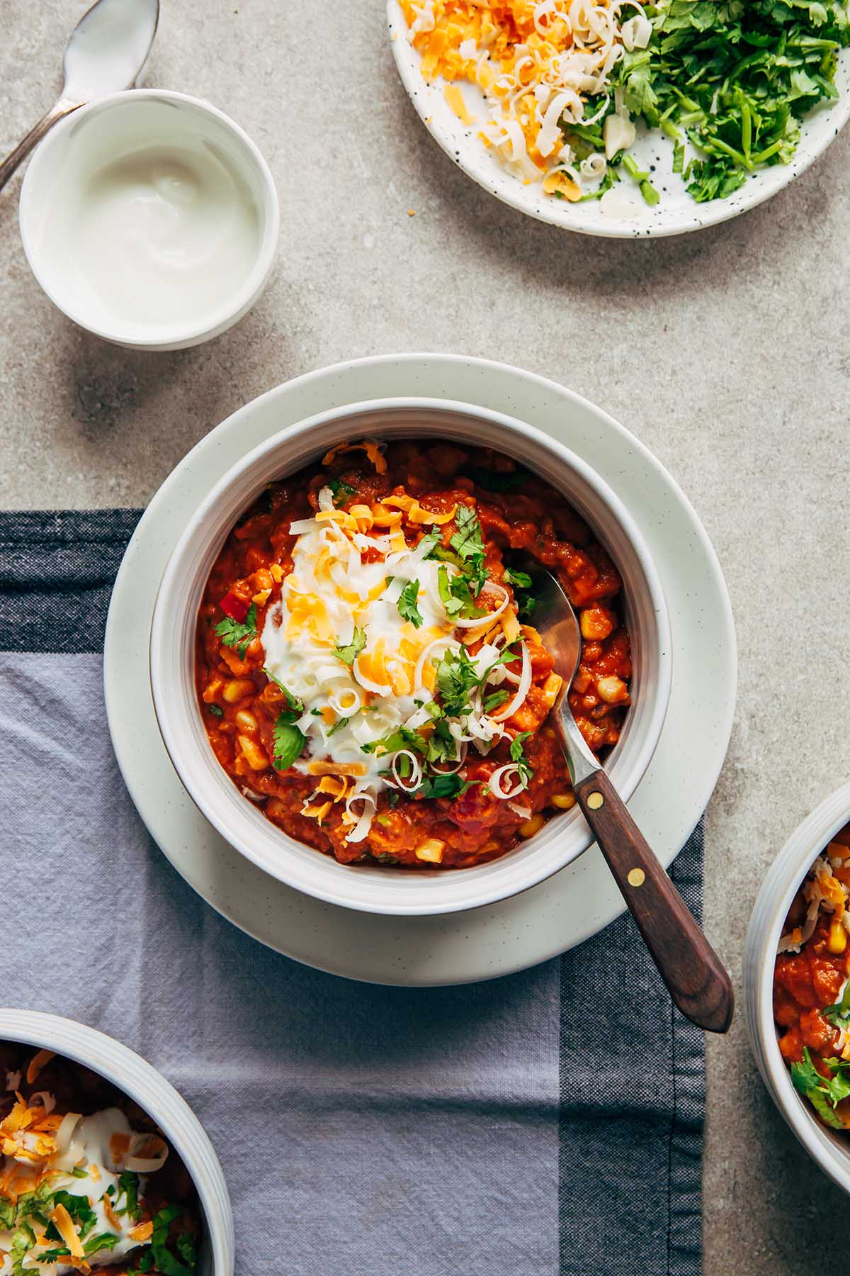 A bowl of coconut milk chili topped with yogurt, cilantro, and shredded cheese.