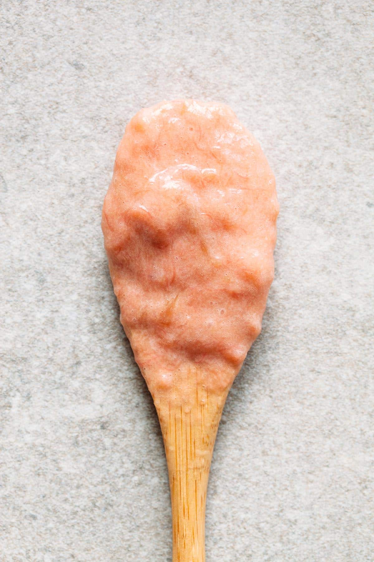 A wooden spoon with rhubarb curd on a stone surface.