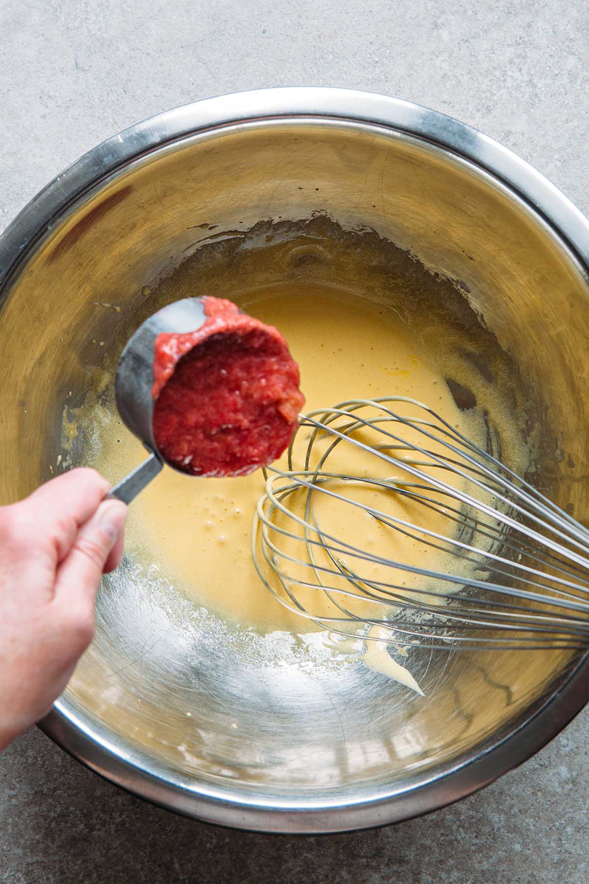 A hand dripping rhubarb curd into whisked egg yolks.