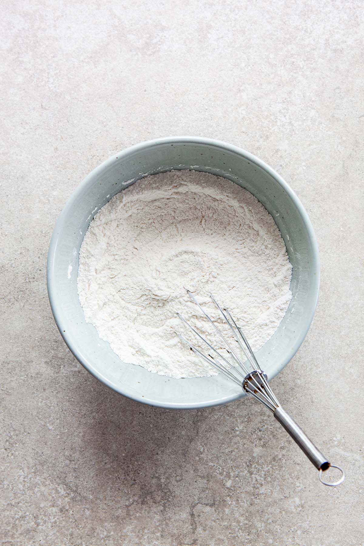 A light blue bowl filled with flour with a whisk in it.