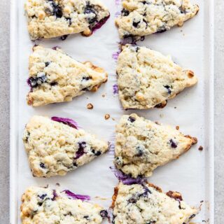 Eight freshly baked triangular blueberry white chocolate scones on a white baking sheet.