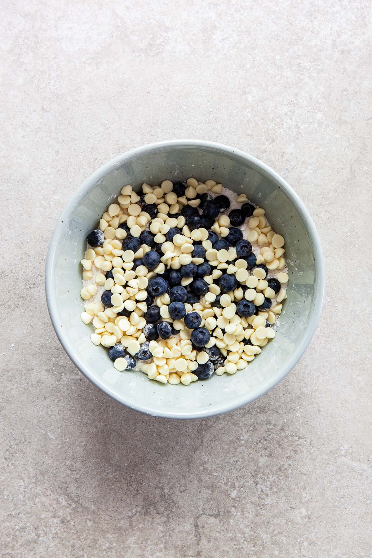 A bowl of flour topped with fresh blueberries and white chocolate chips.