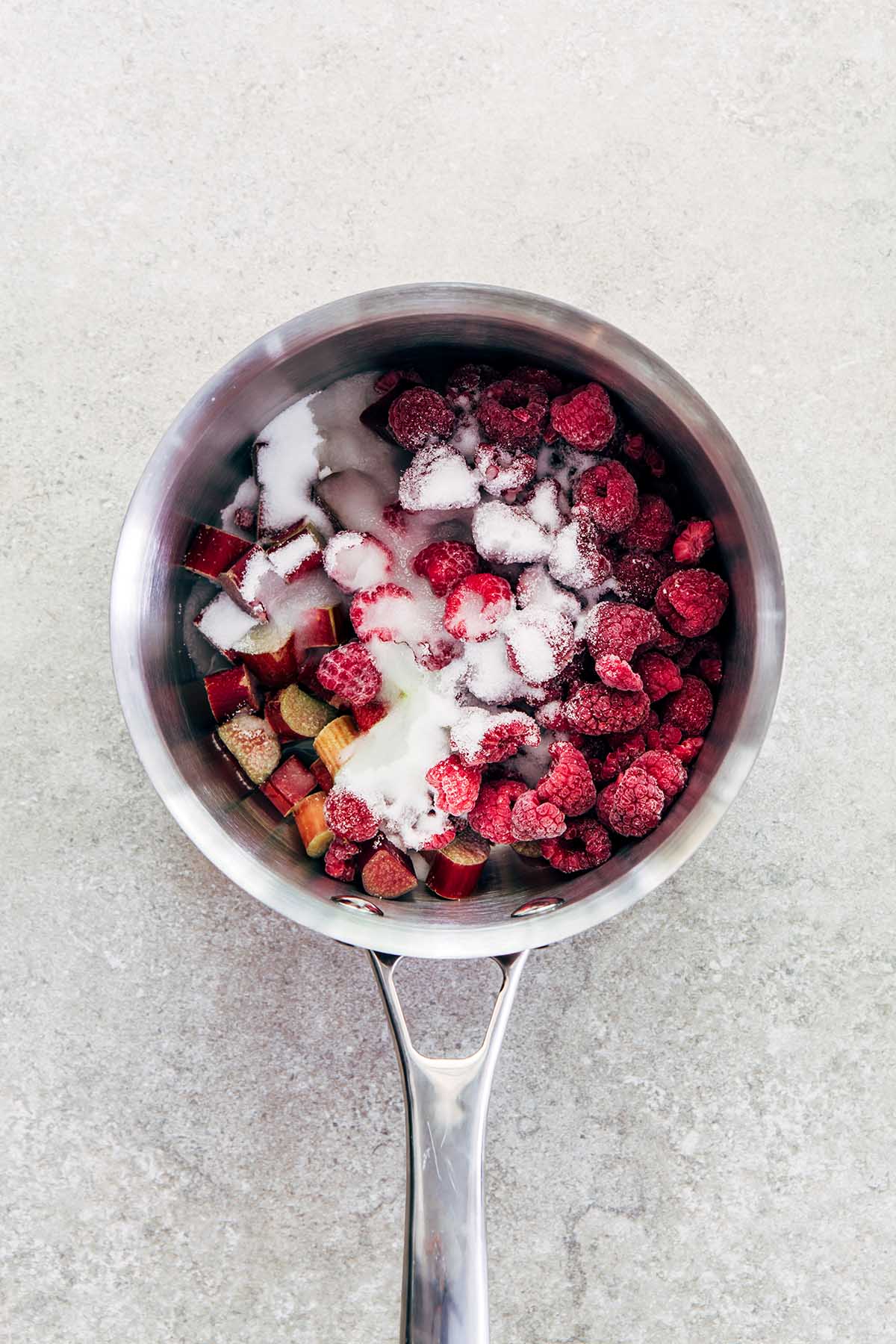 Rhubarb, raspberries, sugar, salt, and lemon juice in a small silver pot from overhead.