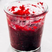 A jar of raspberry rhubarb jam on a table.