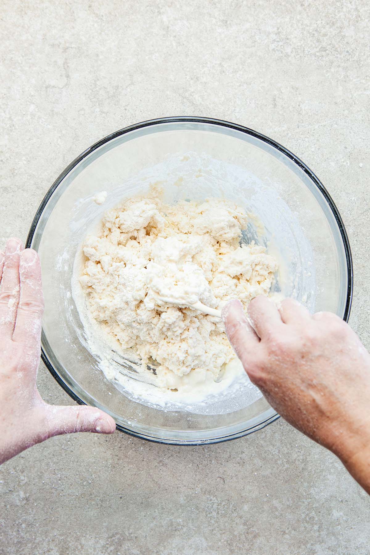 A hand mixing biscuit dough in a glass bowl with a fork.