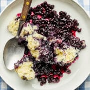 A bowl of Nova Scotia blueberry grunt on a blue and white checked tablecloth.