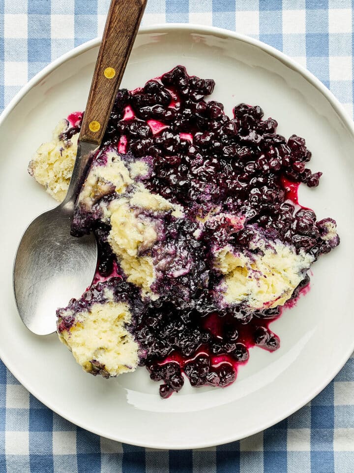 A bowl of Nova Scotia blueberry grunt on a blue and white checked tablecloth.