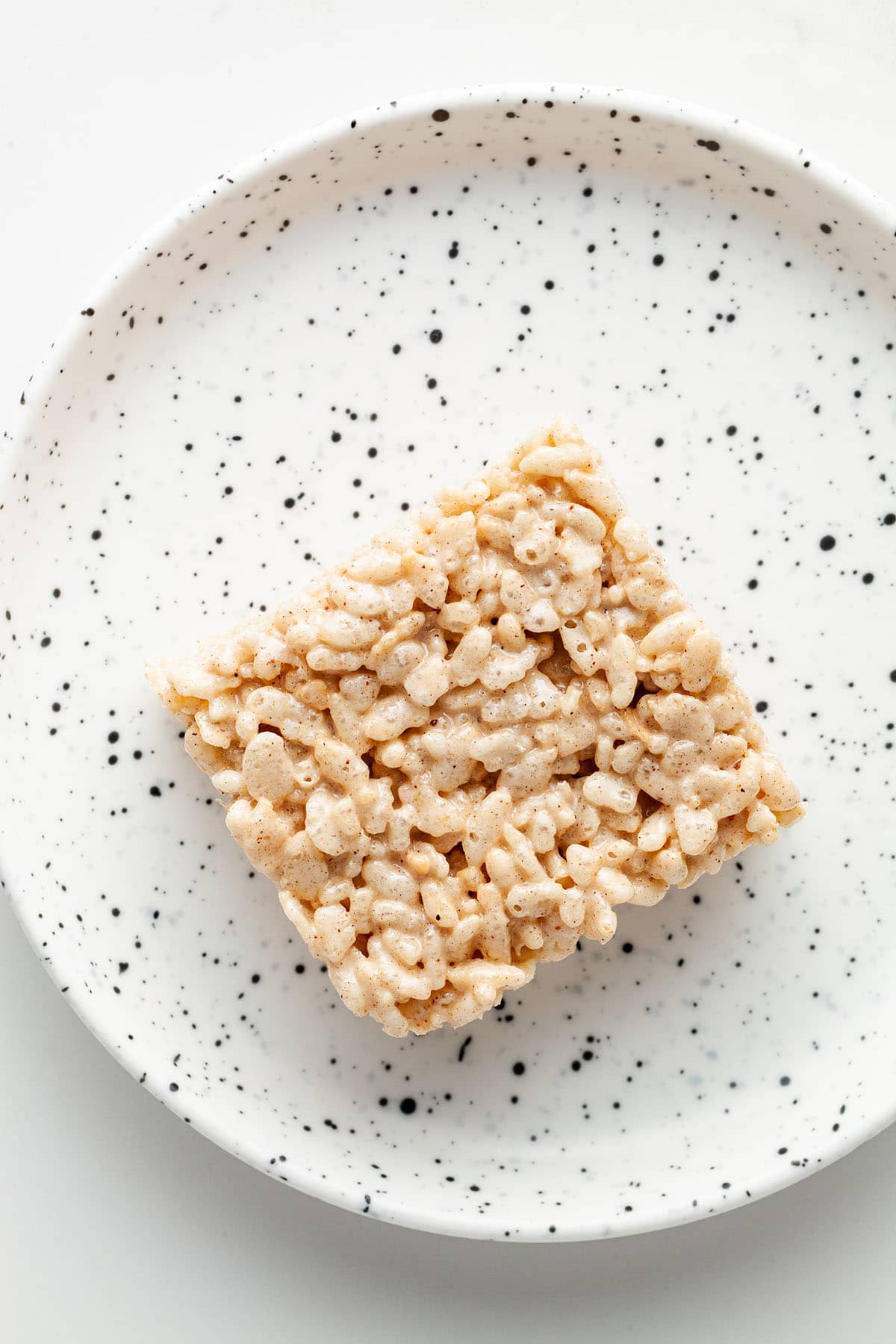 One spiced Rice Krispie treat on a small white speckled plate.