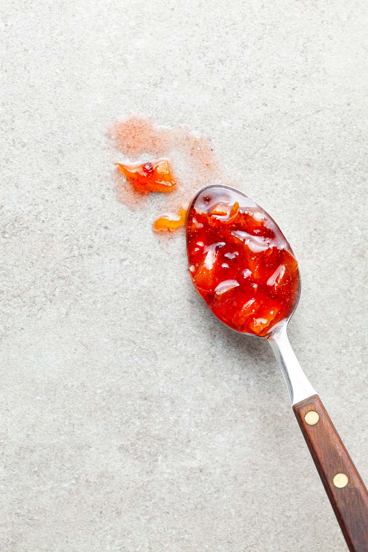 Maple peach whisky jam on a spoon laid out on a stone surface.