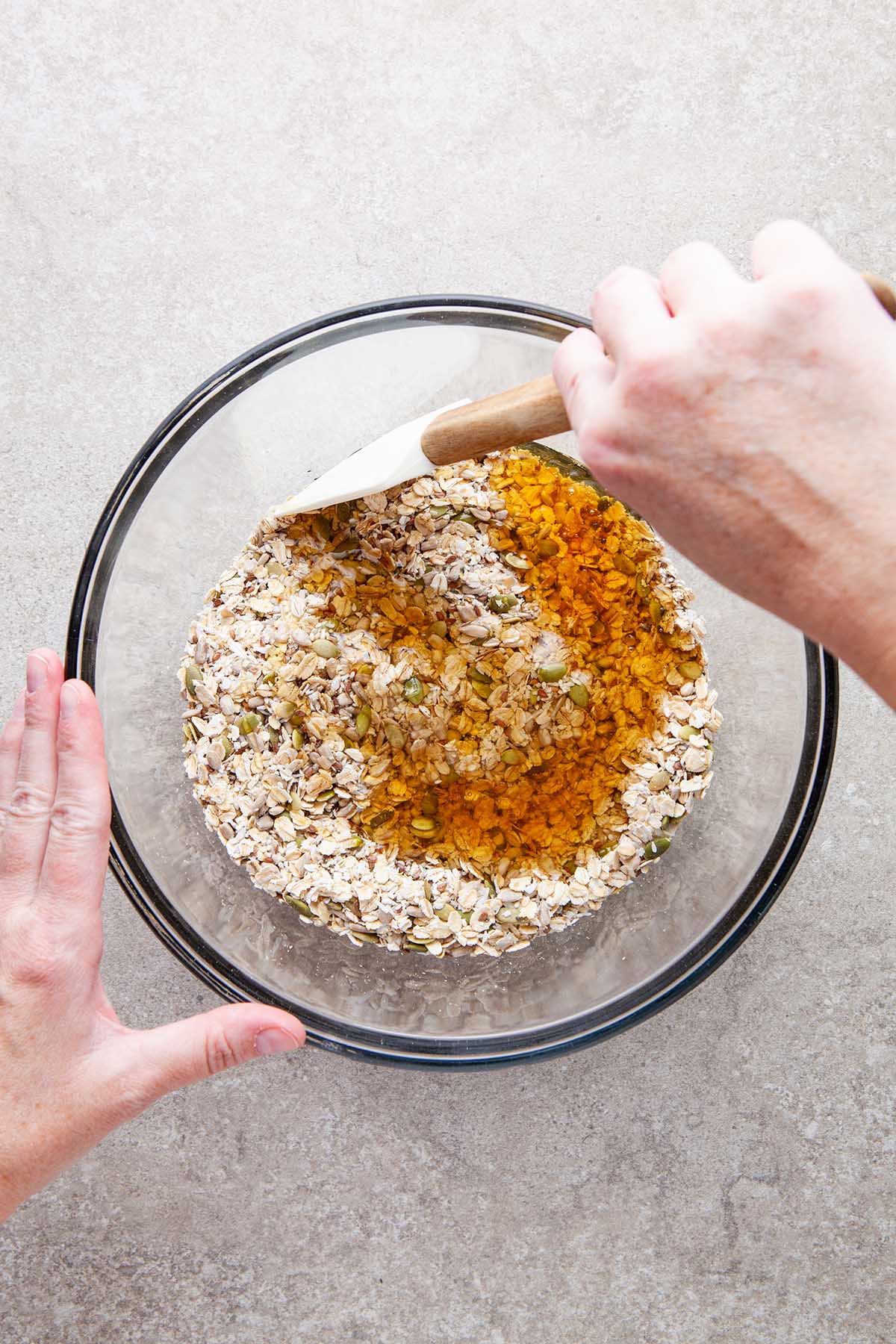 A hand about to stir a bowl of oats, seeds, and honey.