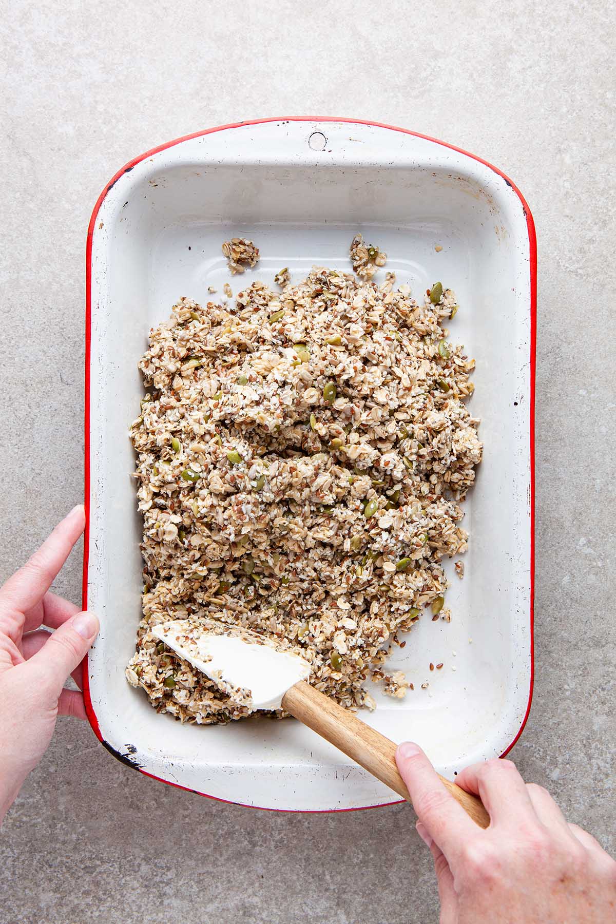 A hand smoothing unbaked granola in a baking dish.