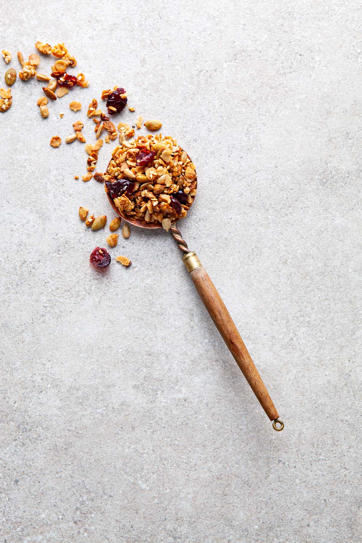A copper spoon on a stone surface with granola spilling out of it onto the stone.