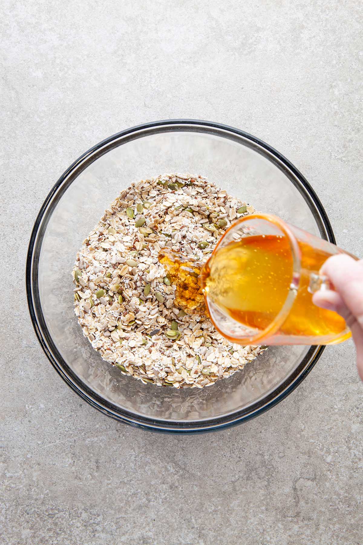 A hand pouring honey into a glass bowl of oats.