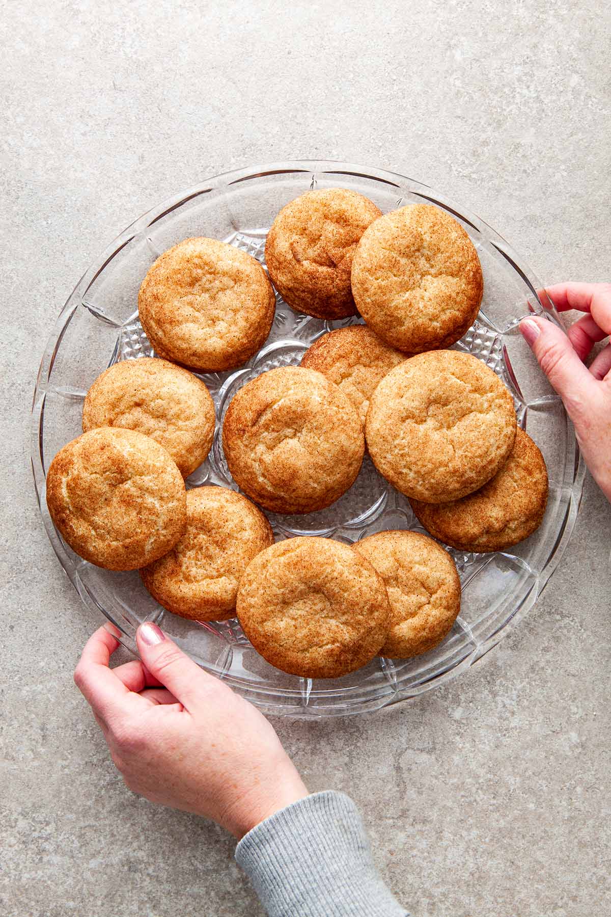 A large glass of platter of snickerdoodles without cream of tartar with two hands holding the edges of the platter.