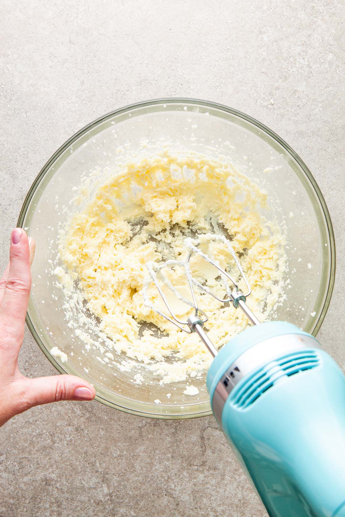 A hand using a hand mixer to cream butter and sugar.