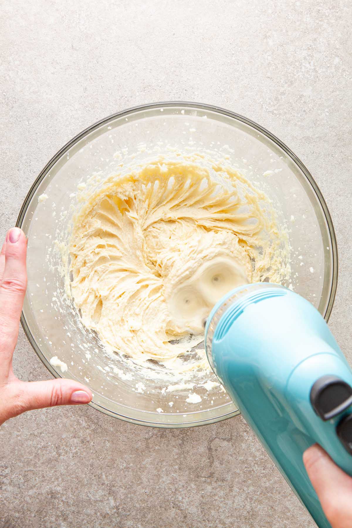 A hand using a hand mixer to cream butter and sugar.