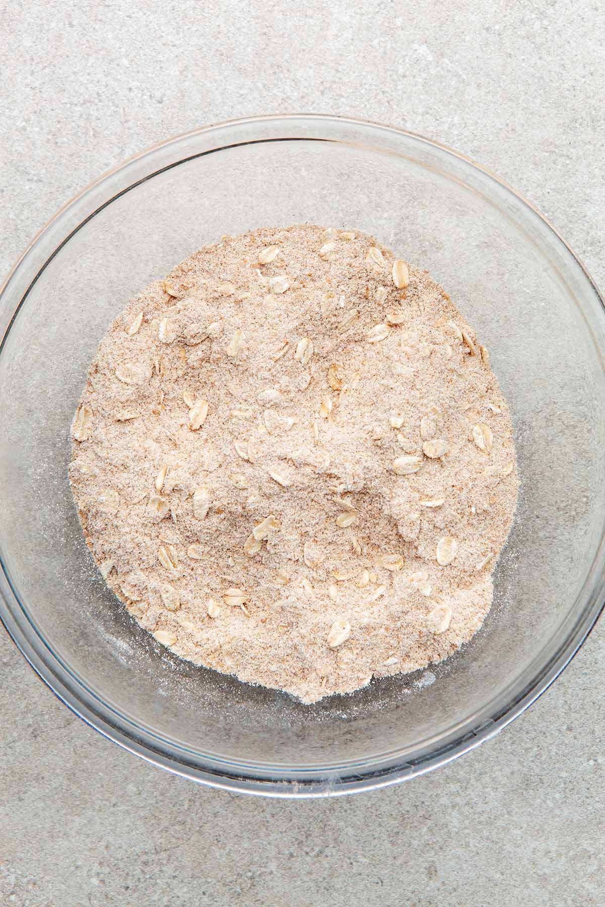 A glass bowl of oats, flour, cinnamon, and brown sugar mixed together.