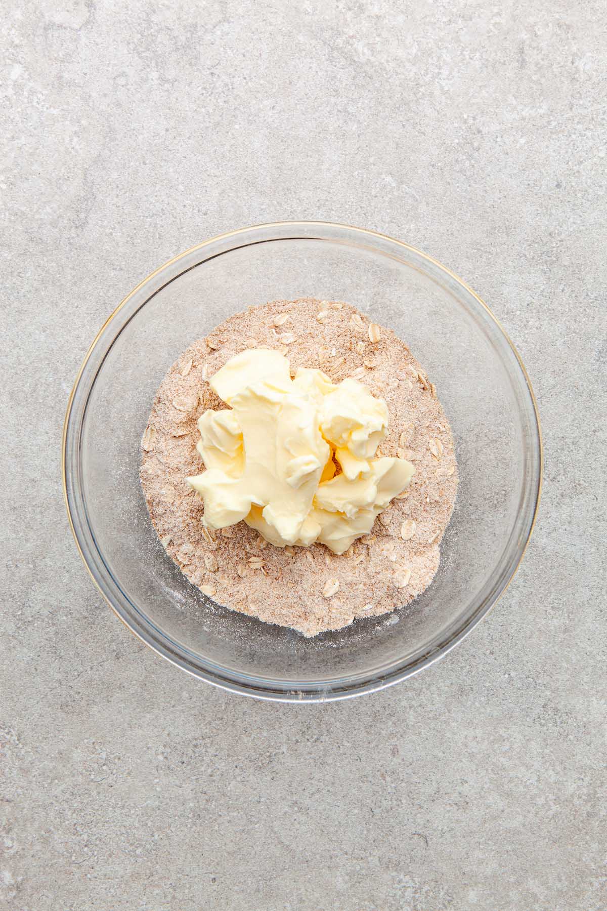 A bowl of flour and oats with a large chunk of butter sitting on top in a glass bowl.