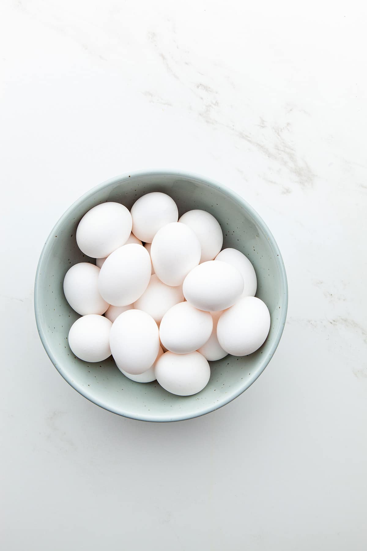 A light blue bowl filled with eggs on a marble surface.