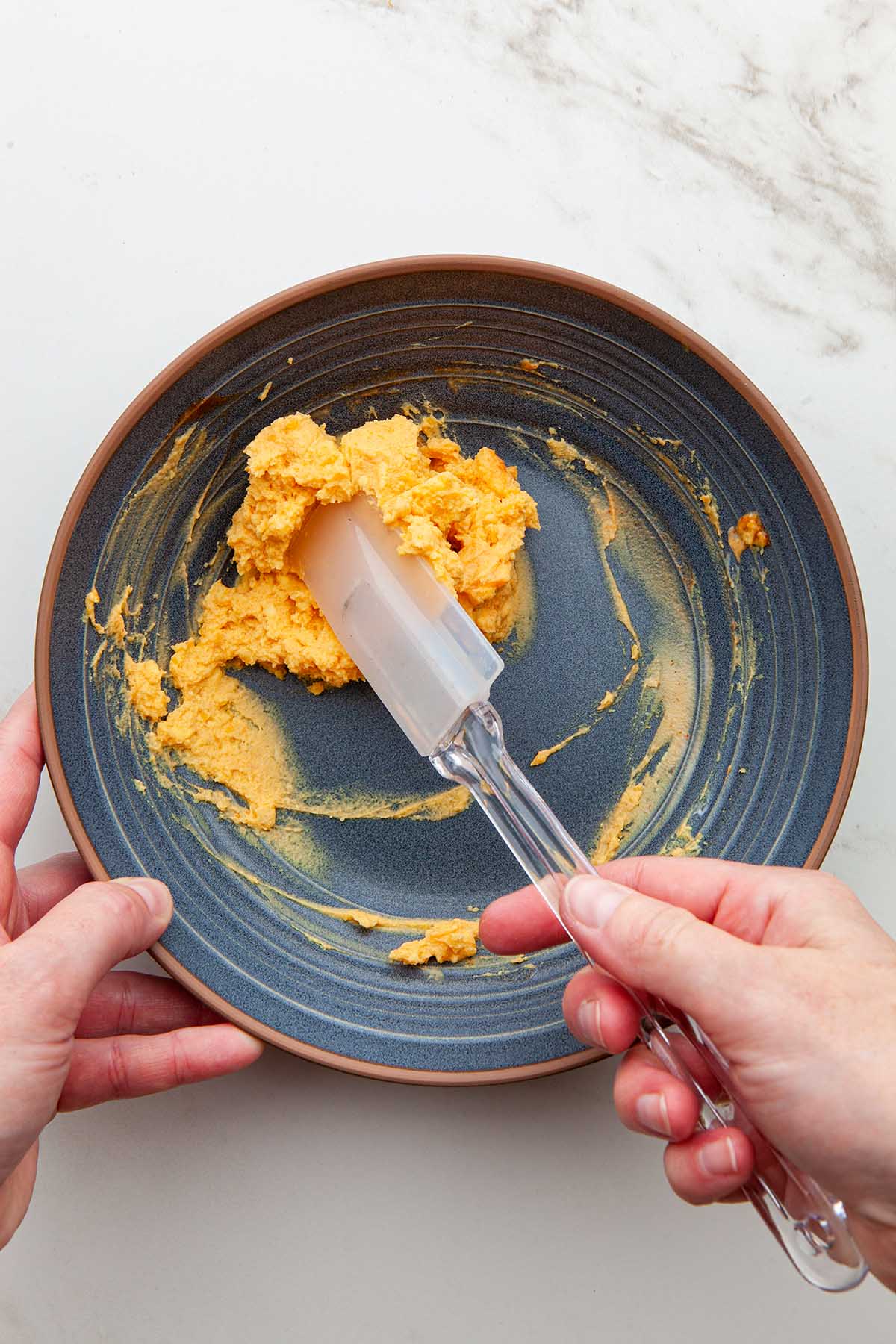 Hands mixing hard boiled mashed eggs yolks with a rubber spatula.