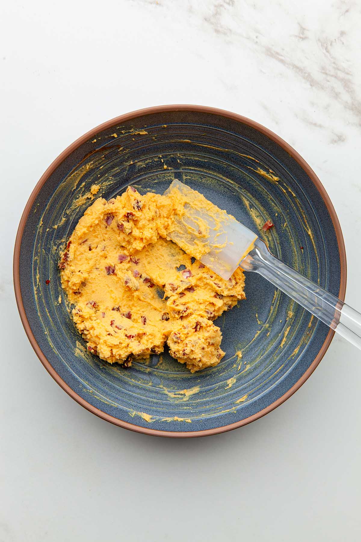 A bowl of mashed egg yolks mixed with finely diced salami and finely diced sun dried tomatoes.
