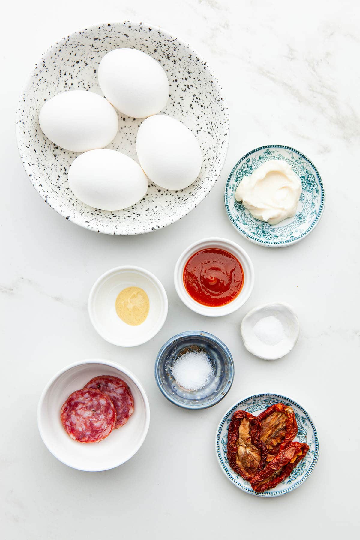 Ingredients to make sriracha deviled eggs laid out in small bowls on a marble surface.