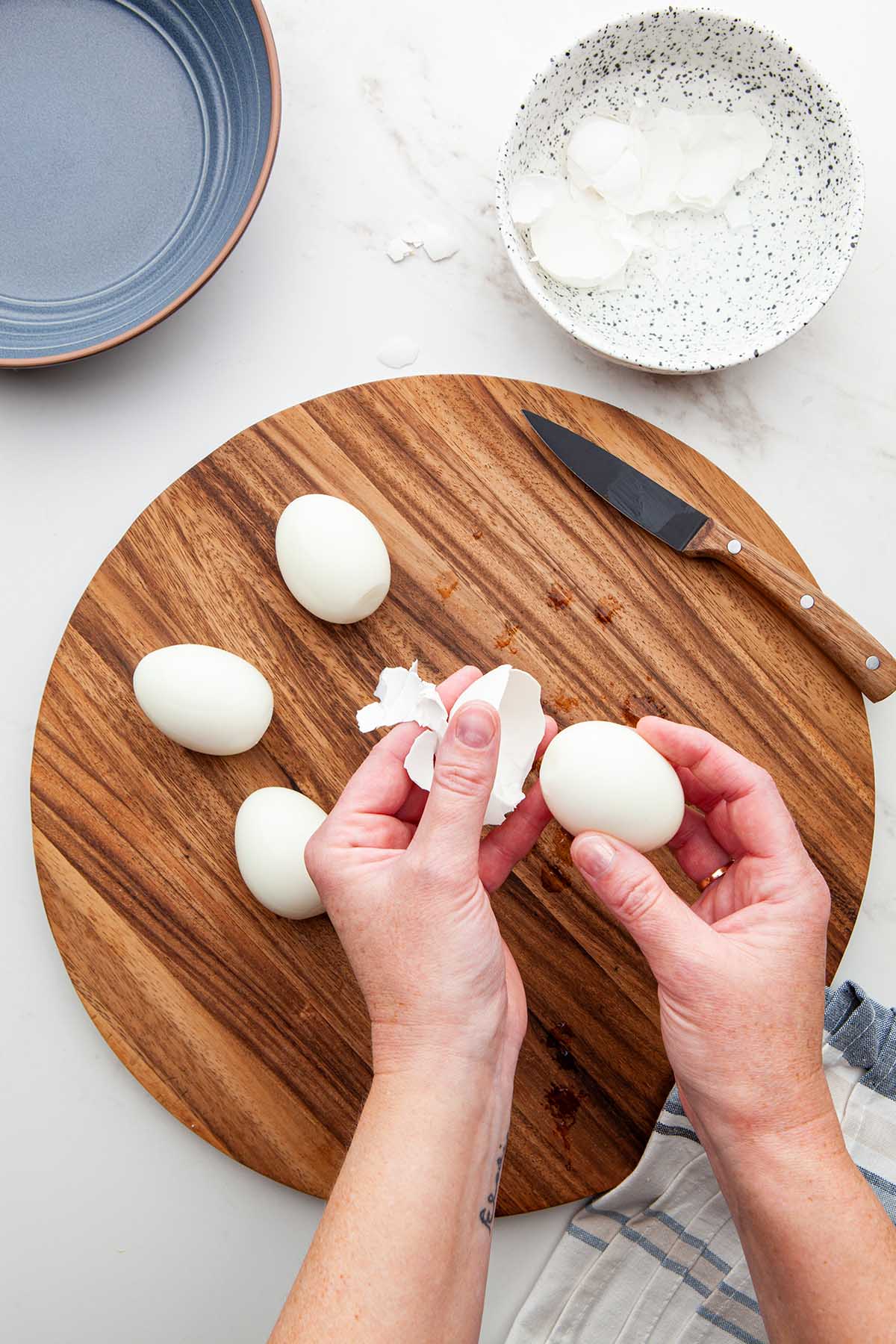 Hands removing the shell from a hard boiled egg.